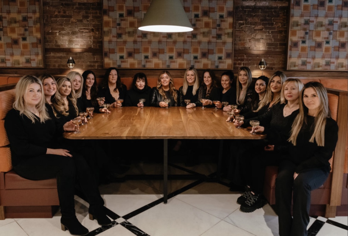 the staff of karasmatic day spa sitting in a half circle around a wood table inserted into a booth